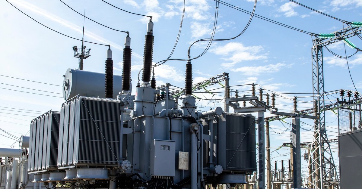 A power plant features a large, high-voltage power transformer. Additional structures uphold power lines.