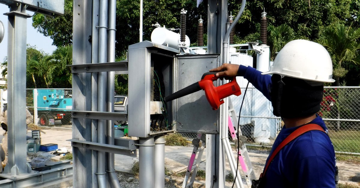 A person wearing a hard hat uses a small handheld vacuum to clean the interior of a power transformer.
